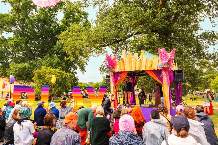 Small wooden round stage with trees in the background, and a small crowd of people sitting in front